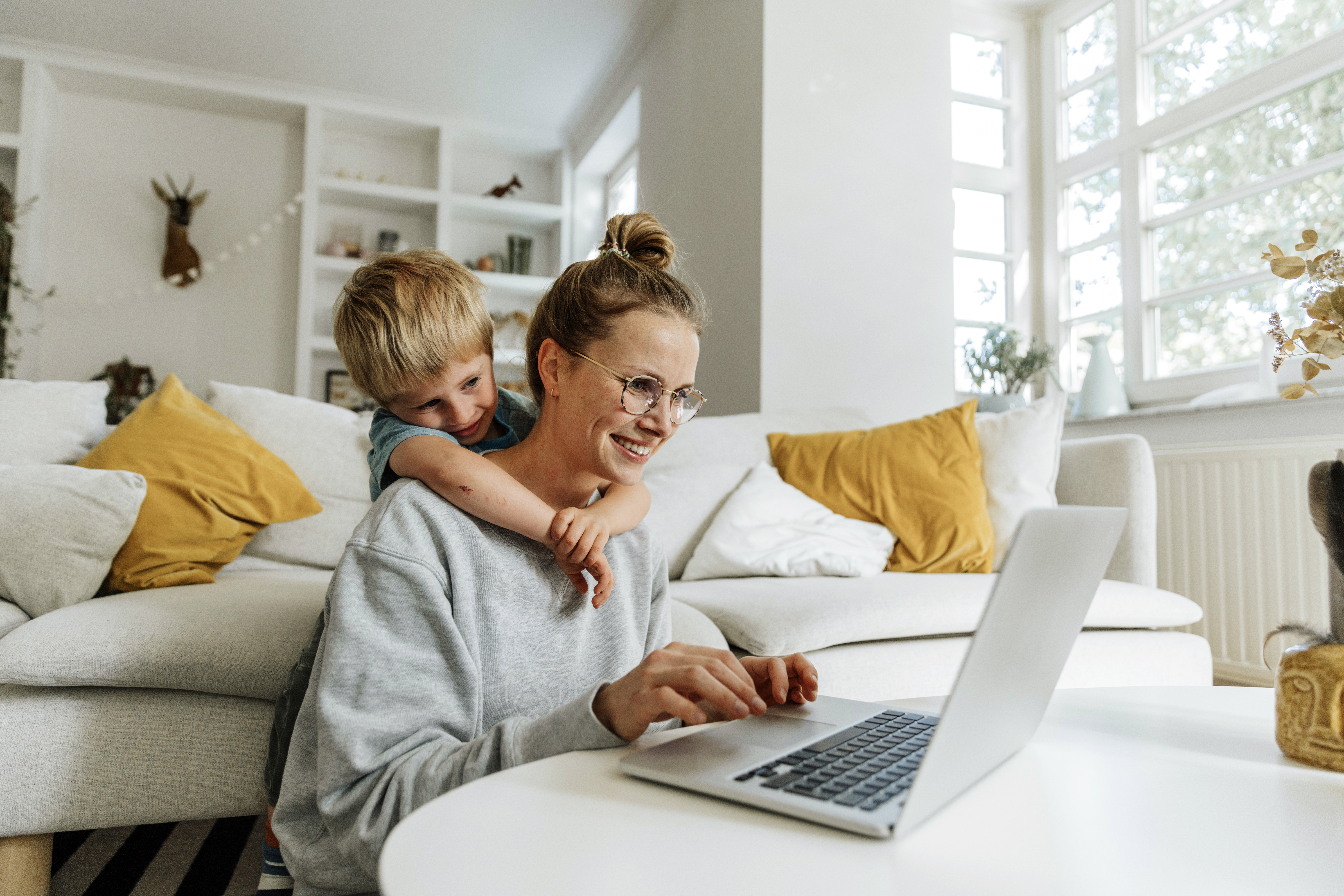 Woman and child using a laptop together in their living room, hugging and smiling